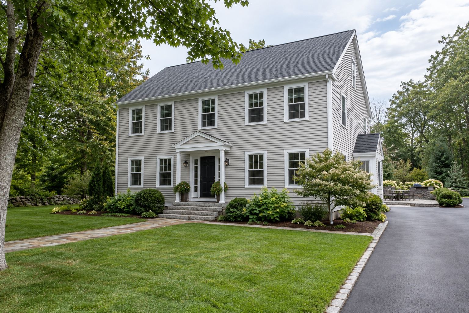 A clean New Hampshire colonial home with its siding, windows, walkway, driveway and patio
